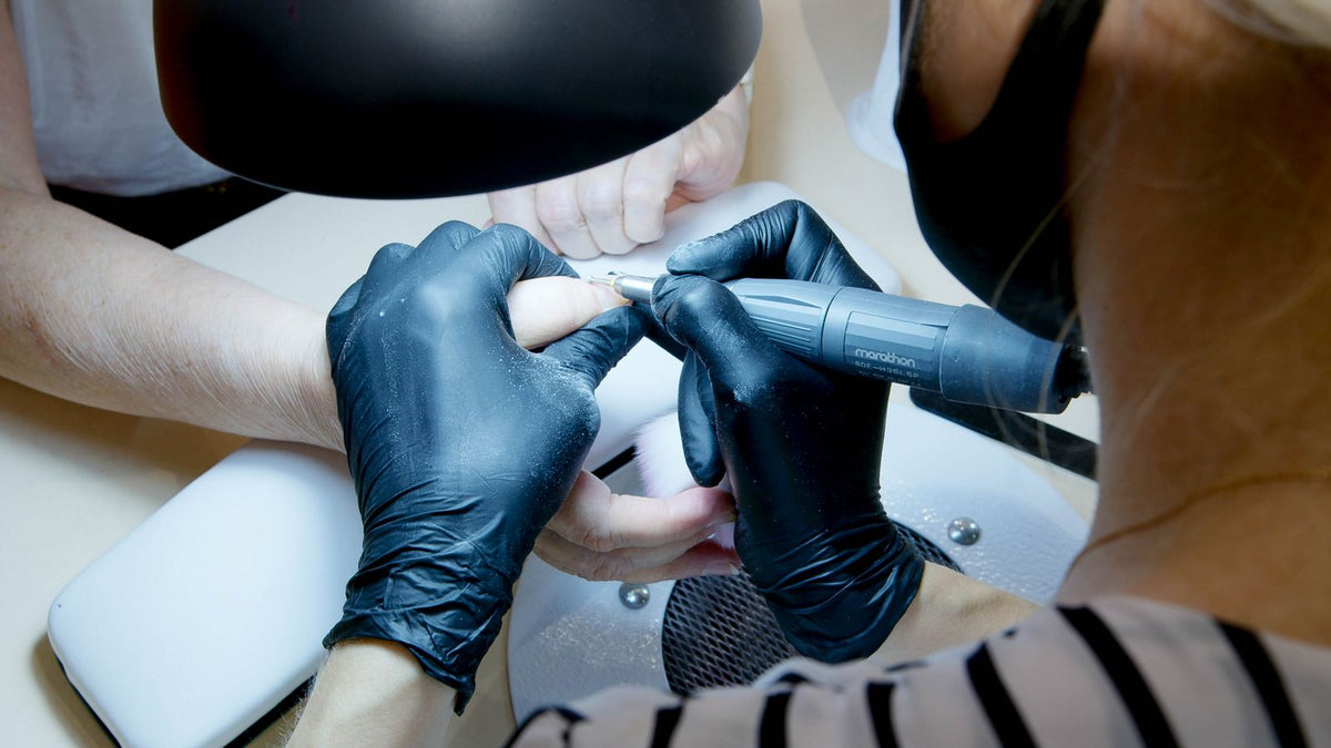 Nail technician in gloves using a Saeyang Marathon nail drill during a manicure